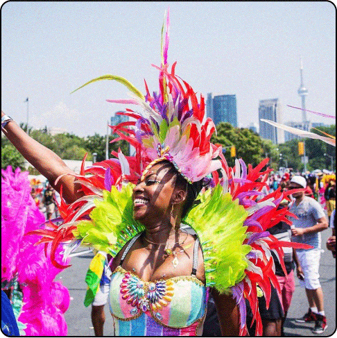 Image Description: A woman wearing a bright feathery costume in a parade smiles big and waves to the crowd.