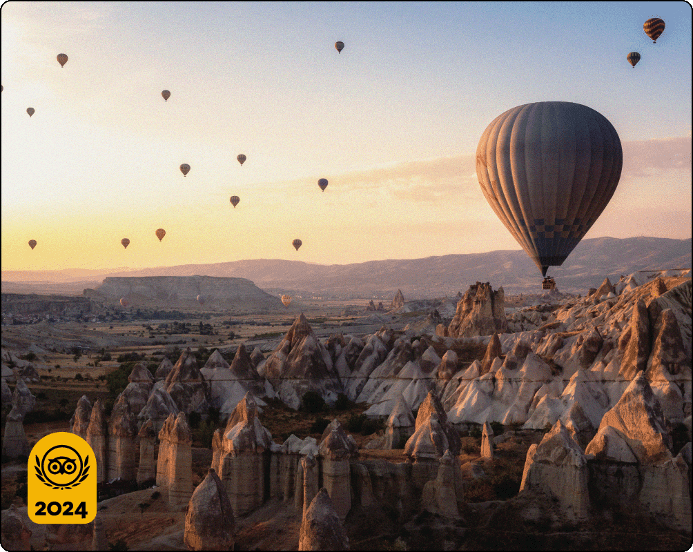 Image Description: A large hot air balloon with smaller hot air balloons in the distance float above rocky spires at sunset.