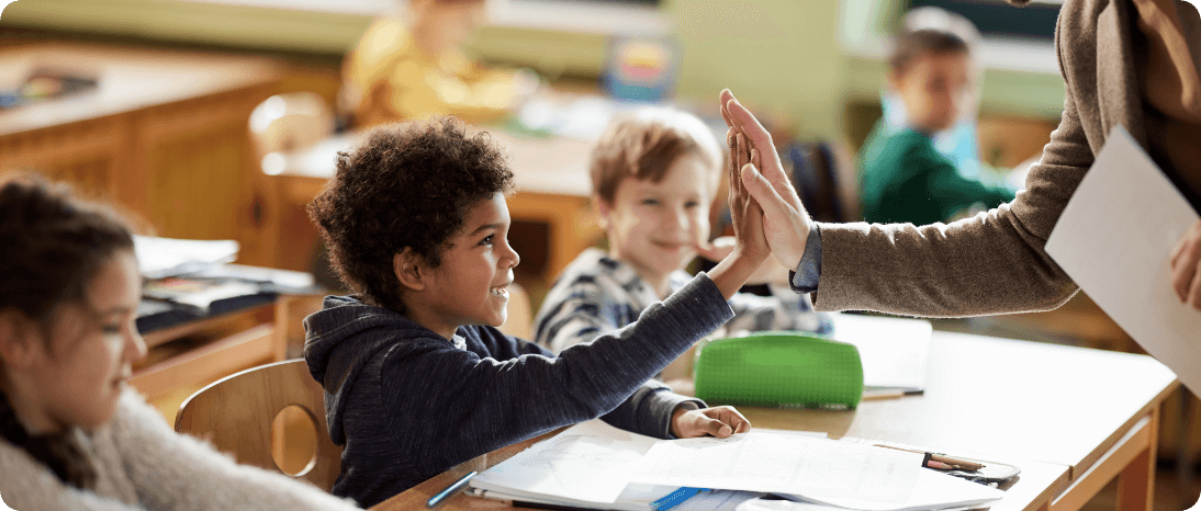 A teacher giving a kid a high-five in a classroom.