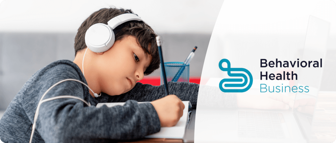 A kid wearing headphones while writing in a book.