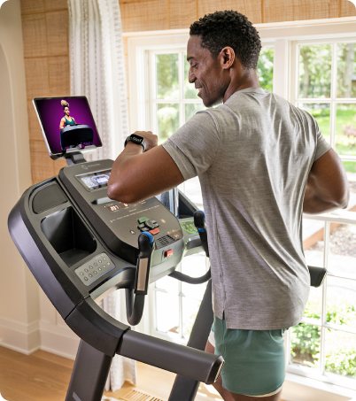 Man running on Horizon treadmill while looking at his connected smart watch Man running on Horizon treadmill while looking at his connected smart watch