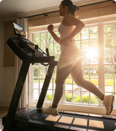 Woman running on Horizon treadmill with sunburst coming through window. Woman running on Horizon treadmill with sunburst coming through window.