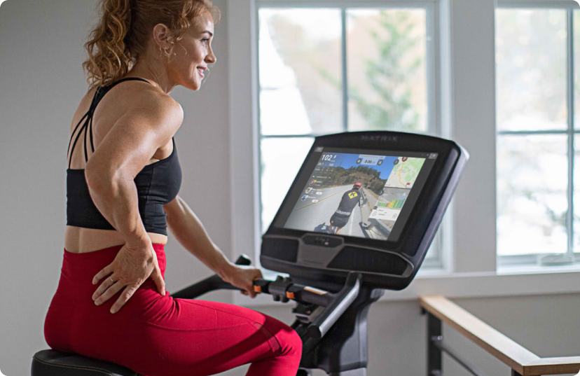 Woman in red leggings riding Matrix upright bike with large display Woman in red leggings riding Matrix upright bike with large display