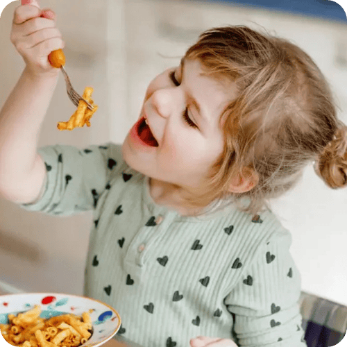 toddler girl eating pasta with tomato sauce