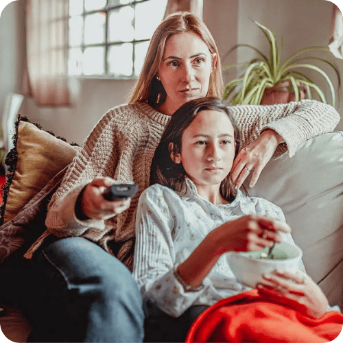 A mom watching tv on the couch with her middle-schooler daughter
