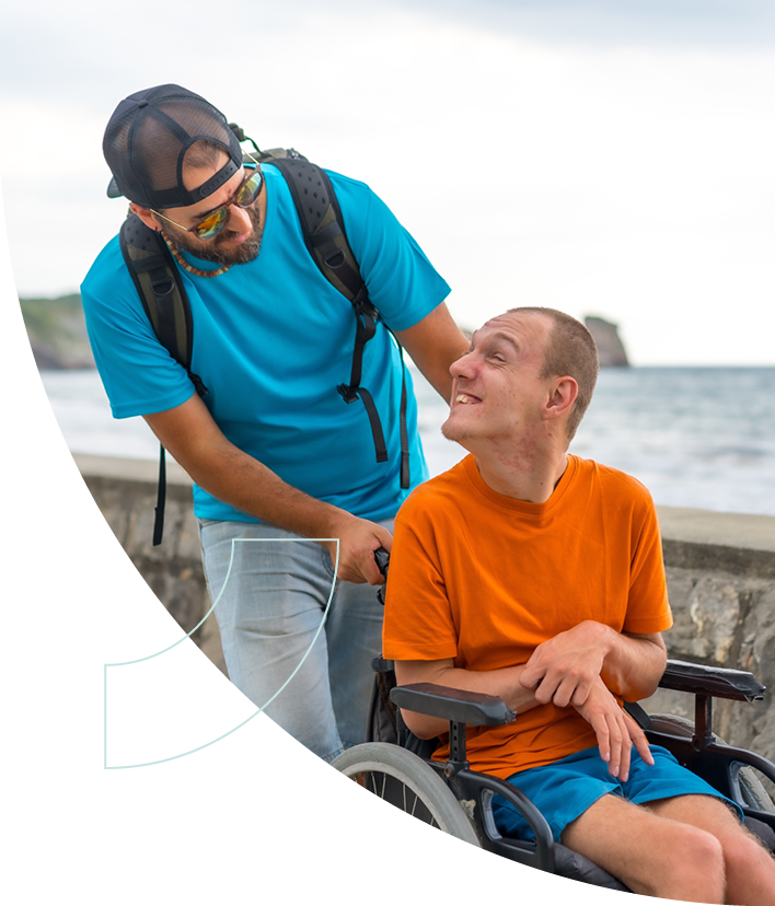 Man in wheelchair smiles at standing man in sunglasses and backwards hat