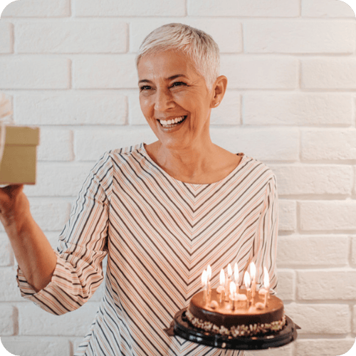 an older woman holding a cake and gift at her grandma shower