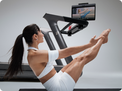 Woman doing yoga pose next to Peloton Tread+