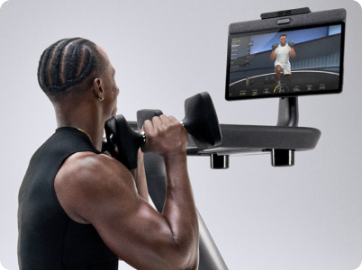 Man doing dumbbell exercises while watching Peloton trainer content