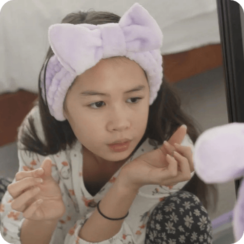 teen doing her skincare routine in the mirror wearing a purple terry headband