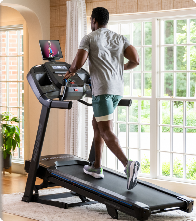 Man running an incline with trainer on Horizon Treadmill in home Man running an incline with trainer on Horizon Treadmill in home