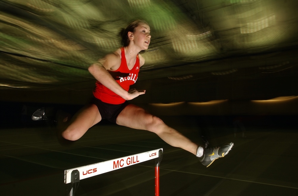 A woman in a McGill shirt jumps a hurdle