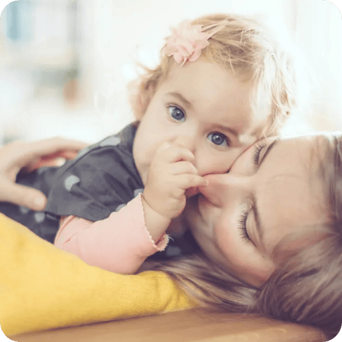 a toddler cuddling her mom while sucking her thumb