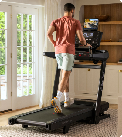 Man in t-shirt and shorts running on BowFlex treadmill in home office