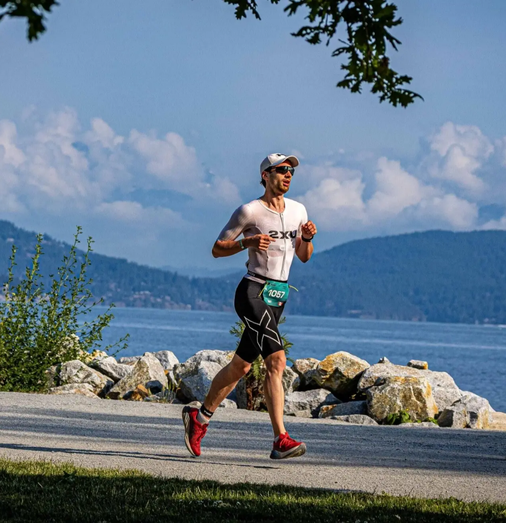 Athlete running along a scenic waterfront course during the Vancouver T100 Triathlon, with ocean and mountains in the background.