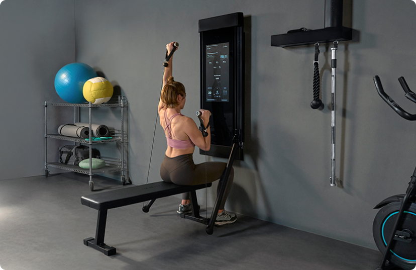 Female athlete doing seated workout on Tonal 2 smart gym in garage
