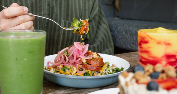 Fork lifting a bite of a vibrant brunch bowl topped with pickled onions and greens at TuRF in Vancouver, alongside a green smoothie and a bright layered drink.
