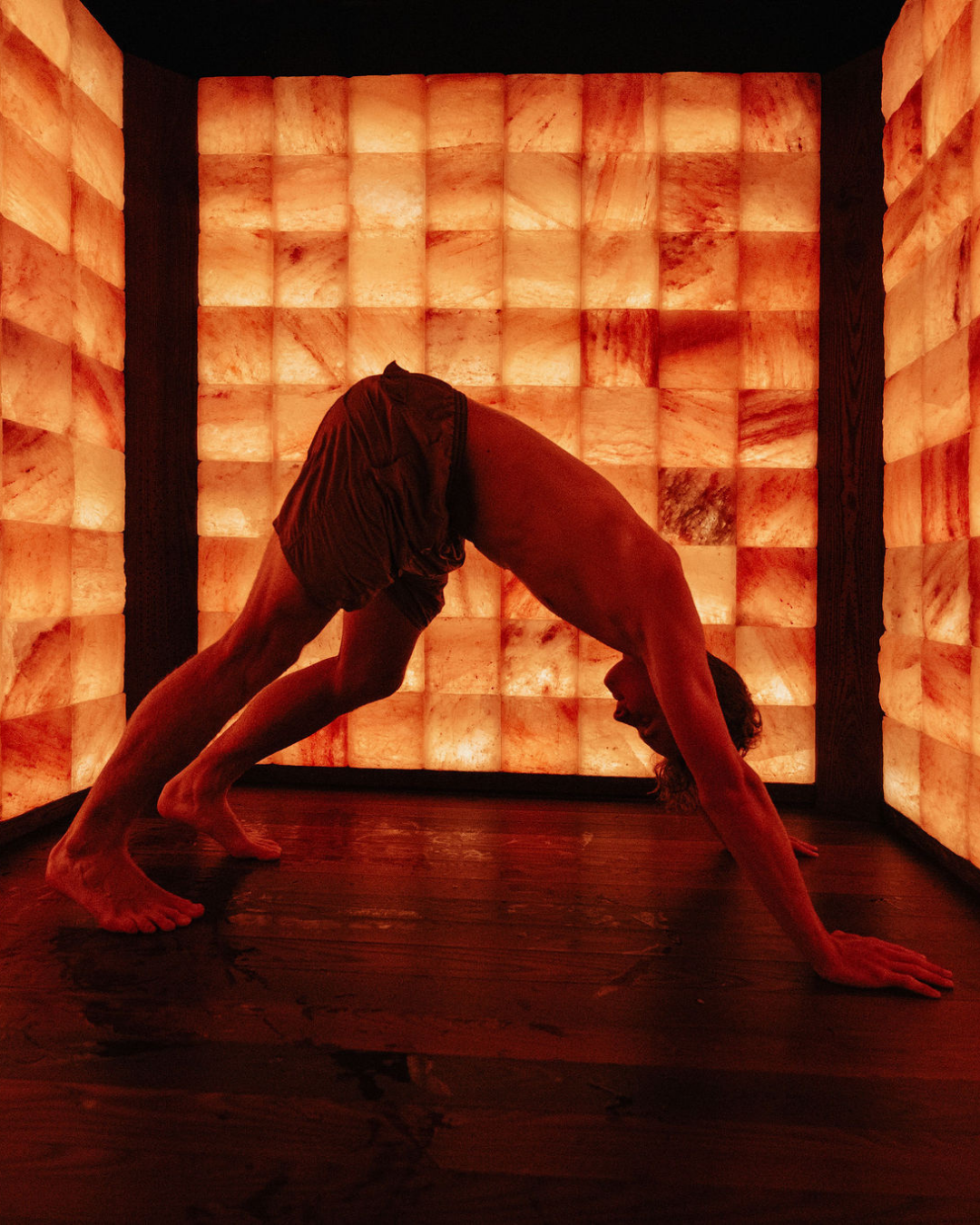 Person in a downward dog yoga pose inside a softly lit Himalayan salt room at Circle Wellness in Vancouver, surrounded by warm amber light.