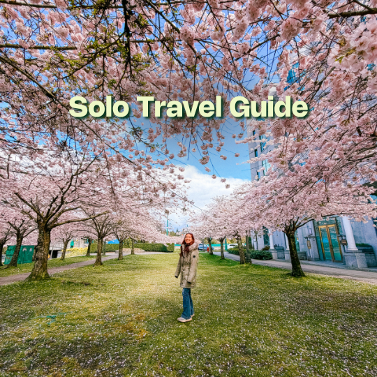 A person stands beneath pink cherry blossoms in a Vancouver park, with petals on the grass and text reading “Solo Travel Guide.