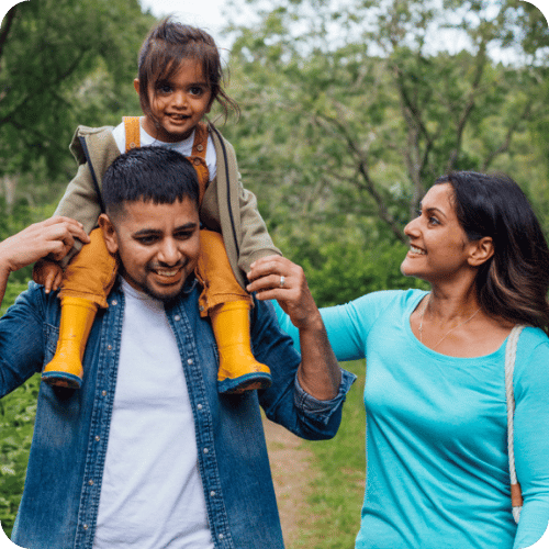 a dad with his toddler daughter on his shoulders beside mom on a neighborhood walk