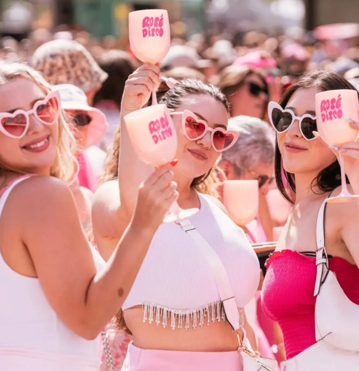 Friends wearing heart-shaped sunglasses and holding rosé glasses at the Rosé Disco Wine Fest in Vancouver.