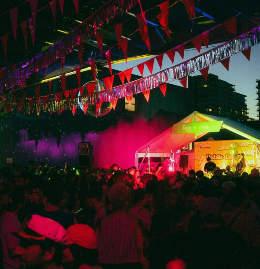 Crowd dancing under colourful lights and festive decorations at the Public Disco Pride Block Party in Vancouver.