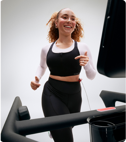 Woman wearing black and white running on Peloton Tread in bright lite studio
