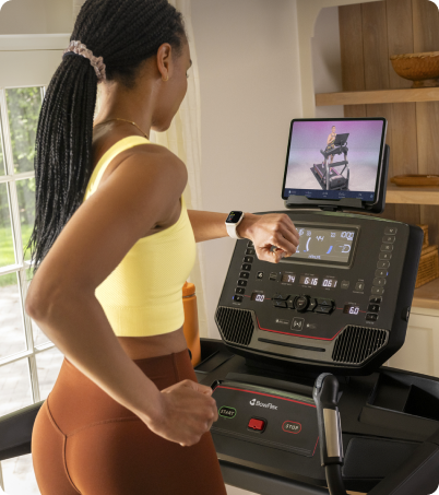 Athletic woman in yellow top using her smart watch with BowFlex T9 Treadmill at home