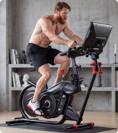 Shirtless man with a beard riding BowFlex VeloCore bike in industrial setting