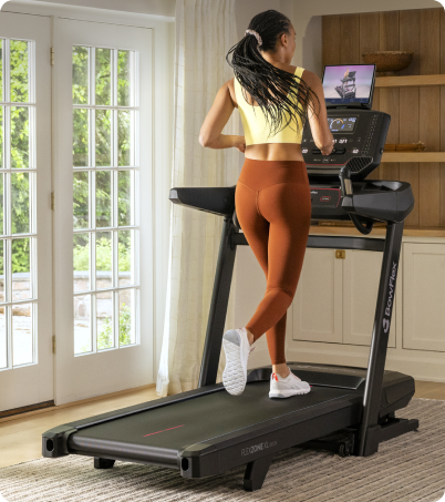 Woman in yellow top and brown leggings running on a BowFlex T9 Treadmill in home