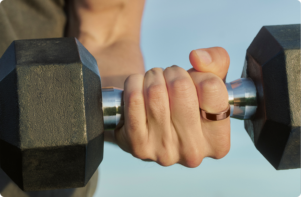 Close-up of a hand wearing a deep rose Oura Ring 5 gripping a dumbbell during a workout