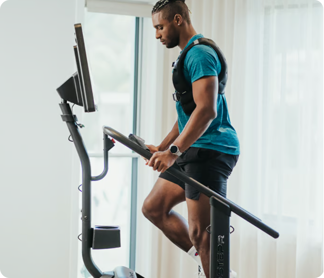 Man climbing on a STEPR machine while wearing a weighted vest.