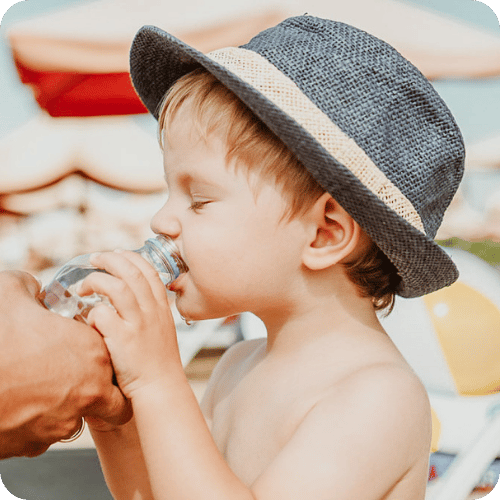 a toddler boy drinking water on the beach