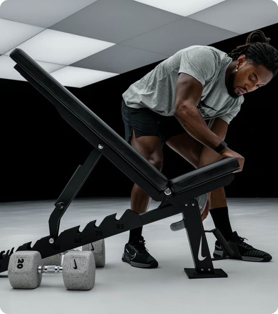 Man adjusting a Nike training bench with dumbbells nearby.