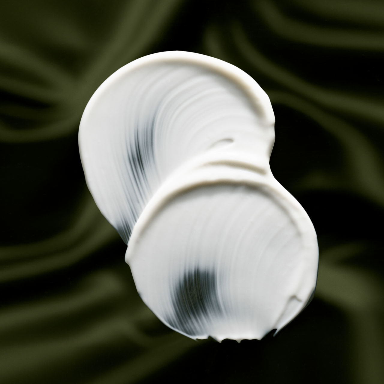 Two rich swirls of white Mega-Mushroom cream on a deep green silk background
