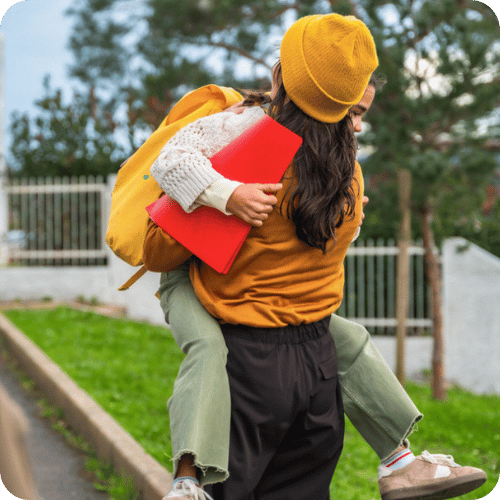mom hugging daughter wearing a backpack outside school