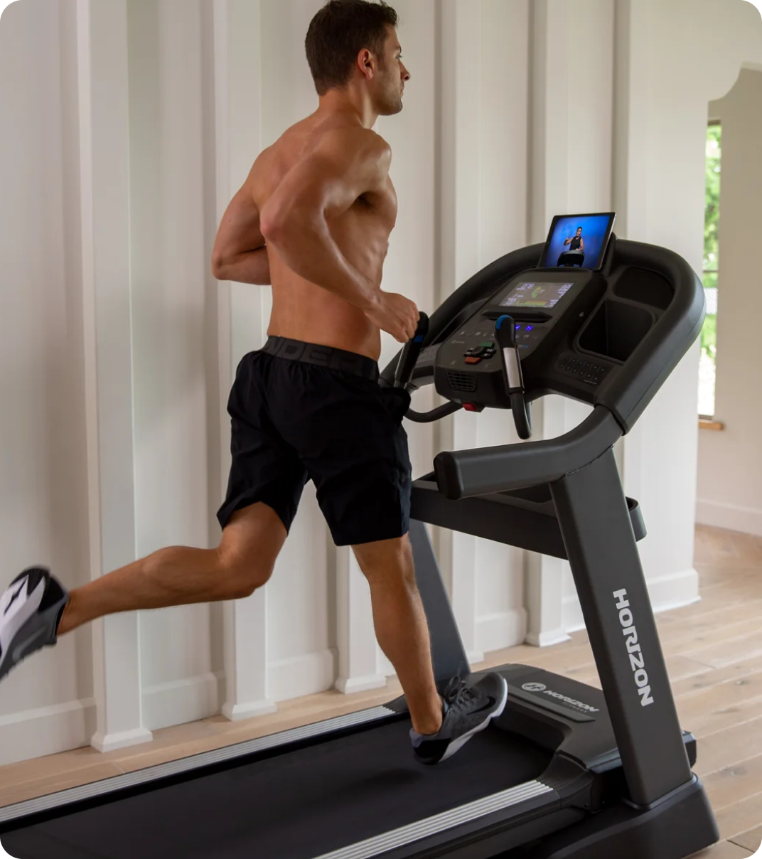 Man running on a Horizon treadmill in a bright home gym. Man running on a Horizon treadmill in a bright home gym.
