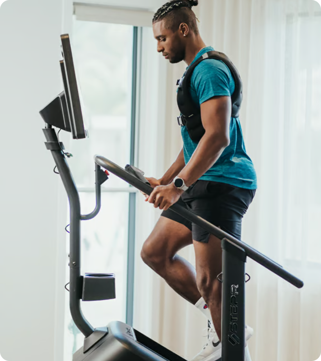 Man training on a STEPR stair climber in a bright home gym. Man training on a STEPR stair climber in a bright home gym.