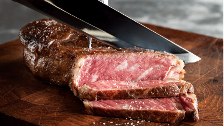 Sliced wagyu beef on wooden cutting board next to chef's knife