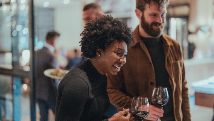 Smiling guests holding wine glasses at an indoor dining event.